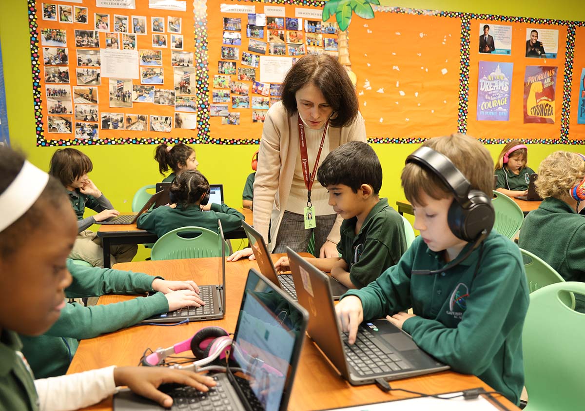 HSA Teacher smiles while kneeling beside a young student in a classroom setting.